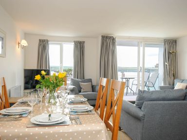 A dining table set with plates and glasses next to a living area with sofas and a TV with windows and a balcony at Slipway 14 in Rock