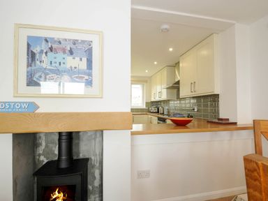 A kitchen with white cabinets and a wooden countertop next to a wall with a fireplace and a framed painting at Slipway 14 in Rock