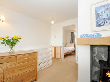 A hallway with a wooden dresser with yellow flowers a white safety gate and a bedroom with a wooden bed and white bedding at Slipway 14 in Rock