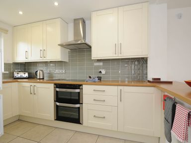 A kitchen with white cabinets a wooden counter tiles on the wall oven and stovetop at Slipway 14 in Rock