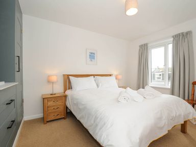 A bedroom with a double bed with white bedding two bedside tables with lamps a window with curtains and a wardrobe at Slipway 14 in Rock