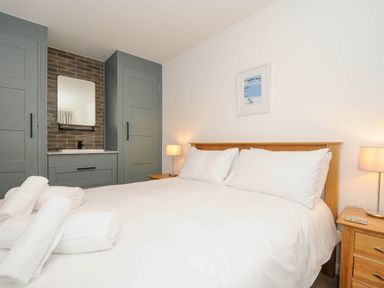 A bedroom with a large bed with white linens two bedside tables with lamps built in cupboards and a sink at Slipway 14 in Rock
