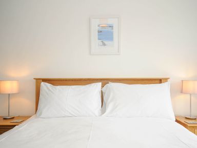 A bedroom with a double bed wooden headboard two white pillows two bedside tables each with a lamp and a framed picture above the bed at Slipway 14 in Rock