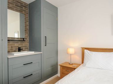 A bedroom with a bed white bedding wooden headboard bedside table lamp and built in wardrobe with sink and mirror at Slipway 14 Rock