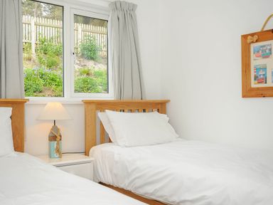 A bedroom with two single beds a nightstand with a lamp a window with curtains and a wall picture at Slipway 14 in Rock