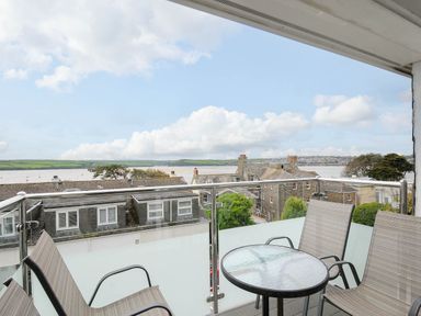 A balcony with a glass table and four chairs overlooking rooftops and a body of water at Slipway 14 in Rock