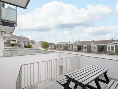 A balcony with a wooden picnic table and a metal railing overlooking neighboring houses at Slipway 14 Rock