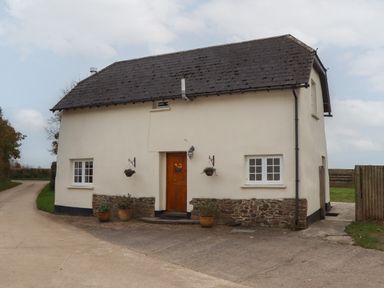 A small cream colored house with a dark roof and wooden door at Cherryblossom Cottage in Winkleigh