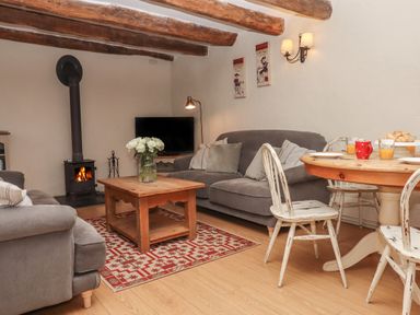 A living room with a wood burner tv grey sofas wooden coffee table white distressed chairs and a round dining table at Cherryblossom Cottage in Winkleigh