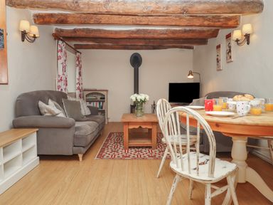 A living room with sofas a wooden coffee table a dining table with chairs and a television at Cherryblossom Cottage in Winkleigh
