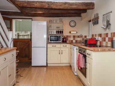 A kitchen with wooden beams and wooden floor with white cabinets and a white refrigerator at Cherryblossom Cottage in Winkleigh