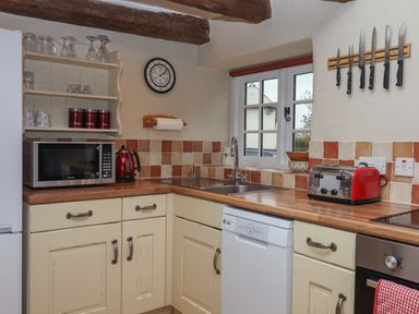 A kitchen with cream cabinets wooden countertop microwave kettle toaster knives and window at Cherryblossom Cottage in Winkleigh