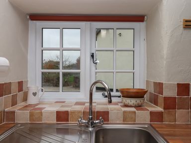 A kitchen sink with a chrome faucet and tiled windowsill with bowls and a jug at Cherryblossom Cottage in Winkleigh