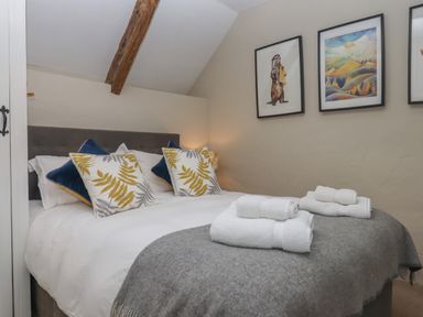 A bedroom with a double bed with pillows and folded towels on a grey blanket and three framed pictures on the wall at Cherryblossom Cottage in Winkleigh