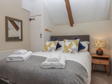 A bedroom with a double bed cushions bedside table and lamp at Cherryblossom Cottage in Winkleigh