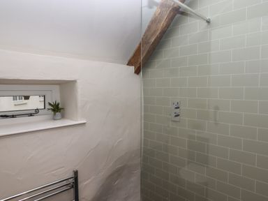 A bathroom with a small window a potted plant a tiled shower wall and a wooden ceiling beam at Cherryblossom Cottage in Winkleigh
