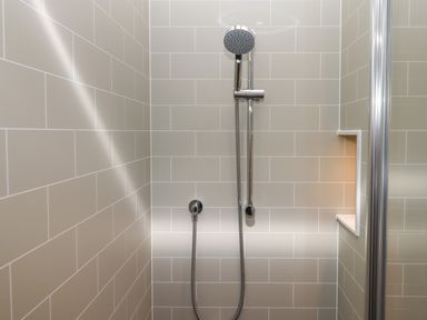 A tiled shower area with a handheld showerhead and a small built-in shelf at Cherryblossom Cottage in Winkleigh
