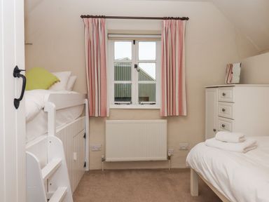 A small bedroom with a bunk bed stairs window with curtains radiator and a chest of drawers at Cherryblossom Cottage in Winkleigh
