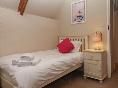 A bedroom with a single bed white bedding red cushion bedside table with lamp and framed picture on wall at Cherryblossom Cottage in Winkleigh