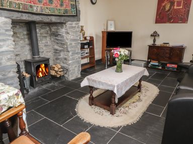 A living room with a stone fireplace and wood stove a coffee table with flowers a television and wooden furniture at Ty Llugwy in Capel Curig near Betws-Y-Coed