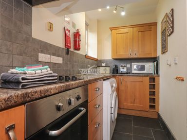 A kitchen with wooden cabinets a washing machine an oven a microwave and a countertop with towels at Ty Llugwy Capel Curig near Betws-Y-Coed