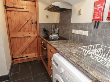 A kitchen with a wooden door stove with utensils washing machine and a dish rack at Ty Llugwy in Capel Curig near Betws-Y-Coed