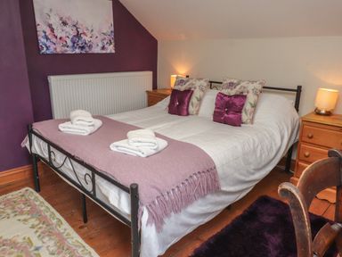 A bedroom with a bed with white bedding and purple pillows and blanket with wooden bedside tables with lamps at Ty Llugwy in Capel Curig near Betws-Y-Coed