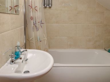 A bathroom with a white sink and faucet next to a bathtub with a shower curtain featuring starfish at Ty Llugwy in Capel Curig near Betws-Y-Coed