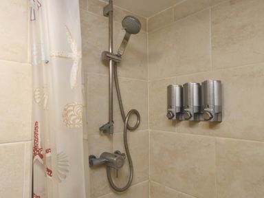 A shower area with a handheld showerhead and three wall-mounted dispensers in a bathroom at Ty Llugwy in Capel Curig near Betws-Y-Coed