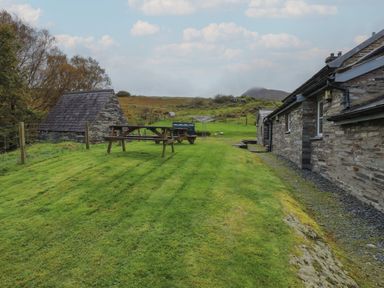 A grassy yard with picnic tables and stone buildings in a rural area at Ty Llugwy Capel Curig near Betws-Y-Coed