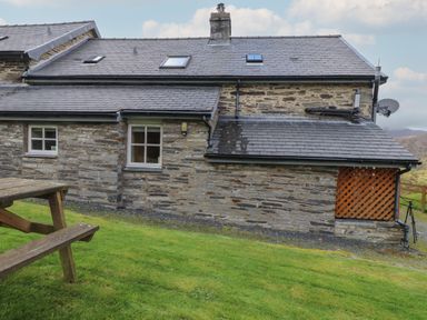A stone house with a slate roof and a wooden picnic table on grass at Ty Llugwy in Capel Curig near Betws-Y-Coed