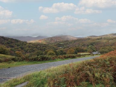 A gravel path running through grassy hills with trees and a mountain range in the background at Ty Llugwy in Capel Curig near Betws-Y-Coed