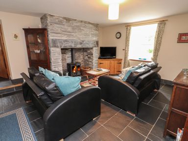 A living room with two black leather sofas and a stone fireplace with a wood stove at Ty Siabod in Capel Curig near Betws-Y-Coed