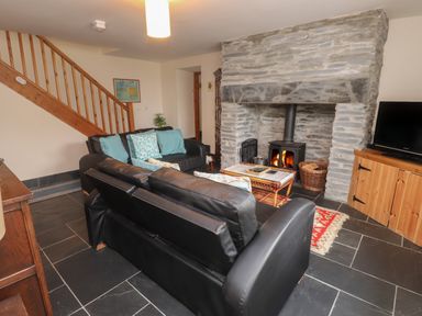 A living room with black leather sofas a stone fireplace a wooden cabinet and staircase at Ty Siabod in Capel Curig near Betws-Y-Coed