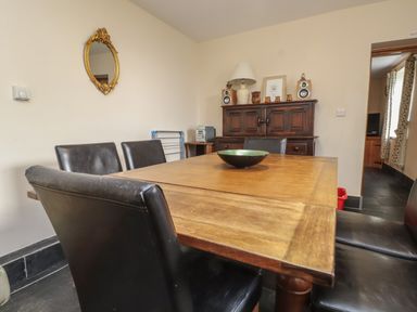 A dining room with a wooden table and black chairs a wooden cabinet with decorative items and speakers on top at Ty Siabod Capel Curig near Betws-Y-Coed