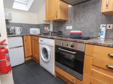 A kitchen with wooden cabinets white washing machine oven stovetop fridge kettle bread box and fire extinguisher at Ty Siabod in Capel Curig near Betws-Y-Coed