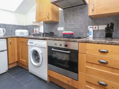 A kitchen with wooden cabinets a washing machine oven and tiled backsplash at Ty Siabod in Capel Curig near Betws-Y-Coed