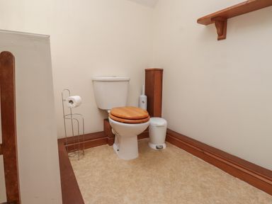 A bathroom with a toilet with a wooden seat a toilet paper holder a toilet brush a small bin and a wooden shelf at Ty Siabod Capel Curig near Betws-Y-Coed