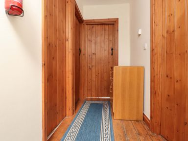 A hallway with wooden panel doors a blue runner rug on wooden floor and a wooden chest of drawers at Ty Siabod in Capel Curig near Betws-Y-Coed