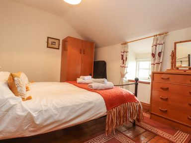 A bedroom with a bed including pillows and folded towels a wooden wardrobe a chest of drawers with a mirror curtains on a window and a rug on the wooden floor at Ty Siabod in Capel Curig near Betws-Y-Coed