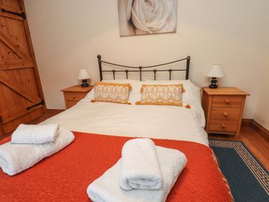 A bedroom with a double bed orange blankets and white towels and wooden bedside tables in Ty Siabod in Capel Curig near Betws Y Coed