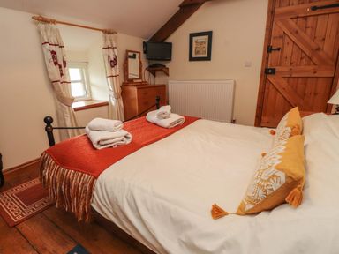 A bedroom with a bed with cushions and towels near a wooden door and window at Ty Siabod in Capel Curig near Betws-Y-Coed