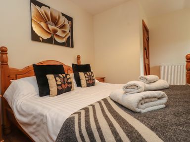 A bedroom with a wooden bed frame pillows rolled towels and a flower painting on the wall at Ty Siabod in Capel Curig near Betws Y Coed