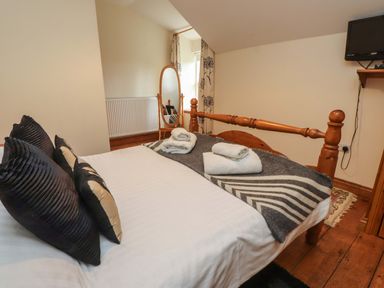 A bedroom with a wooden bed frame black and beige pillows folded towels full length mirror and a wall mounted TV at Ty Siabod in Capel Curig near Betws-Y-Coed
