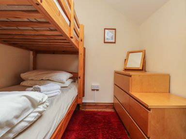 A bedroom with a wooden bunk bed a dresser with a mirror and a red rug on the floor at Ty Siabod in Capel Curig near Betws-Y-Coed