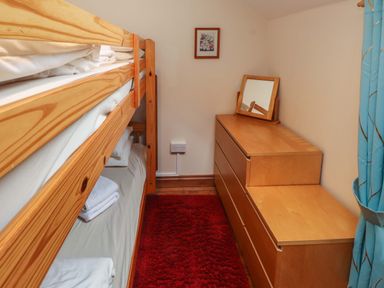 A small bedroom with wooden bunk beds a dresser with a mirror a red rug and blue curtains at Ty Siabod in Capel Curig near Betws-Y-Coed