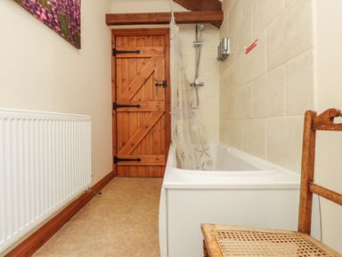 A bathroom with a bathtub a shower curtain a wooden door a radiator and a wooden chair at Ty Siabod in Capel Curig near Betws-Y-Coed