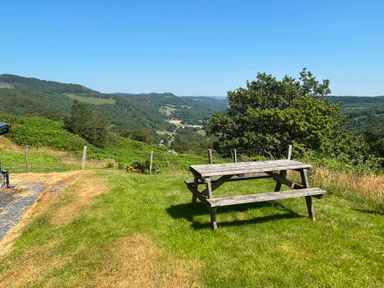 A picnic table on grass with trees and mountains in the background at Ty Siabod, Capel Curig near Betws-Y-Coed