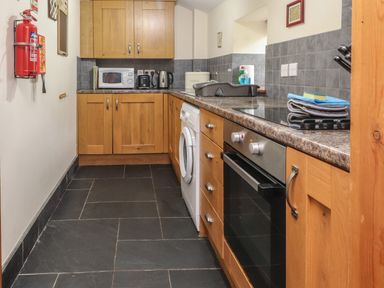 A kitchen with wooden cabinets a washing machine an oven microwave kettle and fire extinguisher at Ty Llewelyn Capel Curig near Betws Y Coed