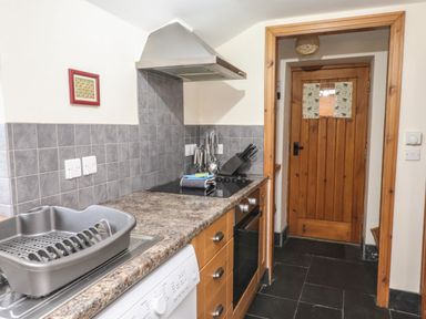 A kitchen with a sink and dish rack oven stove wooden door and tiled backsplash at Ty  Llewelyn in Capel Curig near Betws-Y-Coed